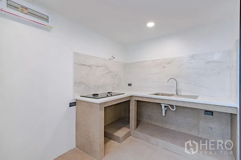 Townhouse for sale - Compact corner kitchen with stone countertops, sink, and electric cooktop.