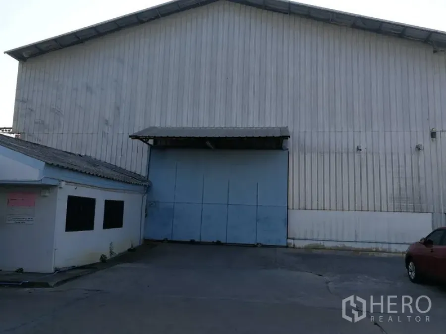 Warehouse for rent in Prawet, Bangkok - Corrugated-metal warehouse exterior with wide blue sliding door, covered loading bay, and driveway access.