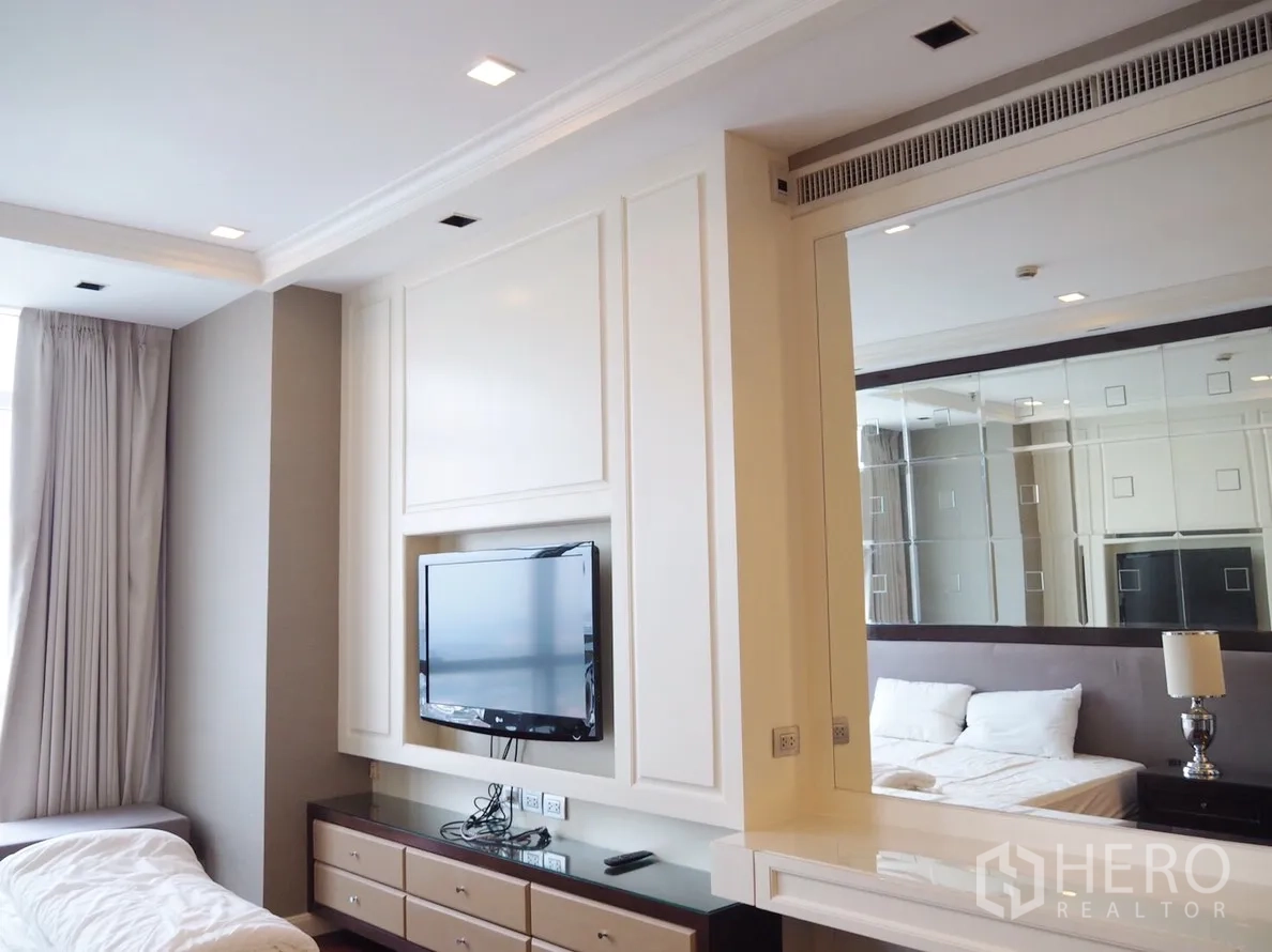Condominium for rent in Pathum Wan, Bangkok - Spacious bedroom with mounted TV, mirrored feature wall and a long cabinet with drawers.