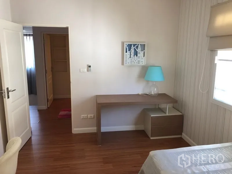 Detached House for rent in Bang Kapi, Bangkok - Cozy bedroom area with study desk, side table and neutral wallpaper.