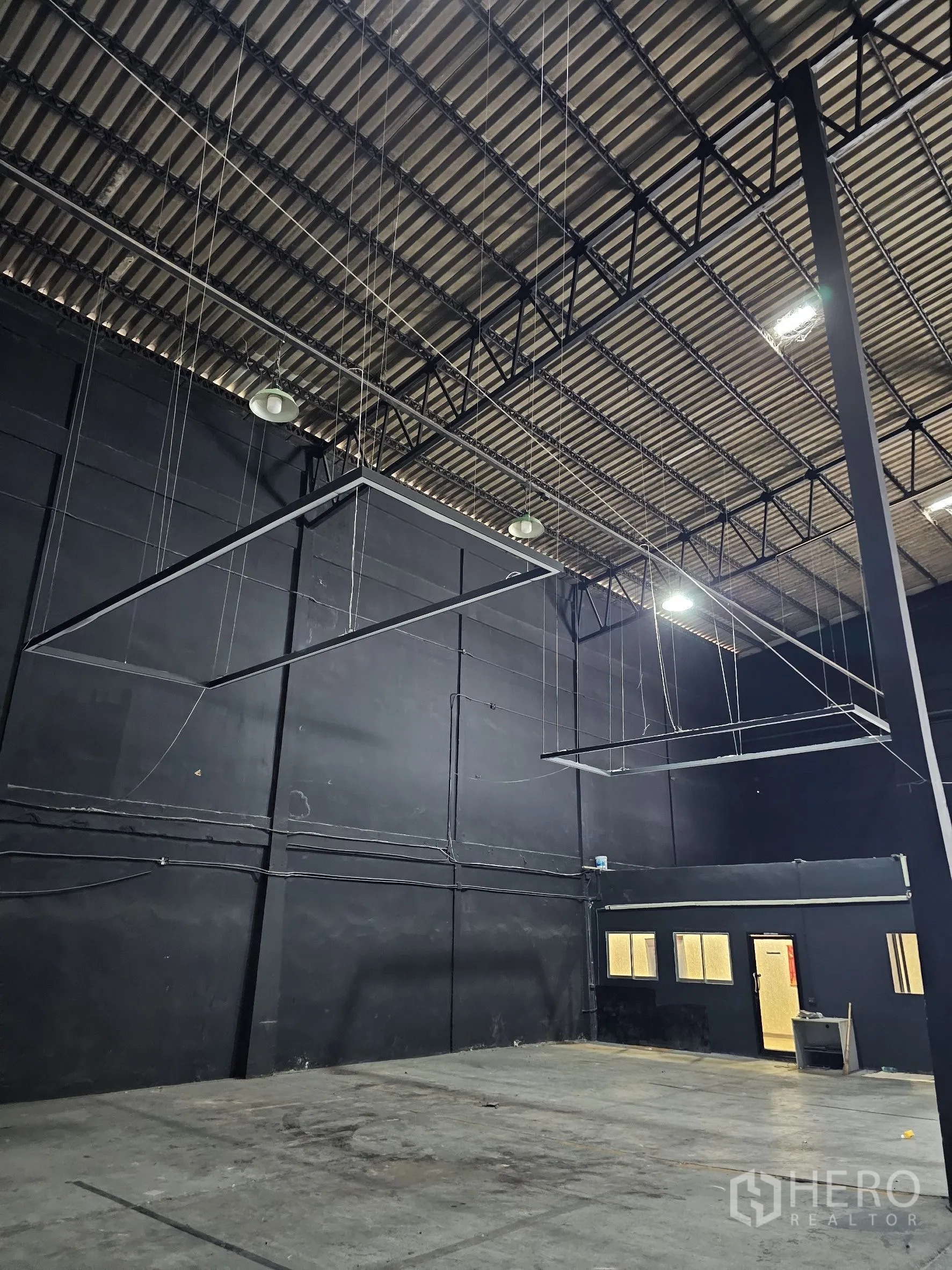Warehouse for rent in Khlong Toei, Bangkok - High ceiling structure with hanging frames, lights, and steel trusses above the floor.