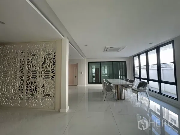 联排别墅 出租在Watthana, Bangkok - 开放式餐区，长餐桌、整面窗与雕花隔断。