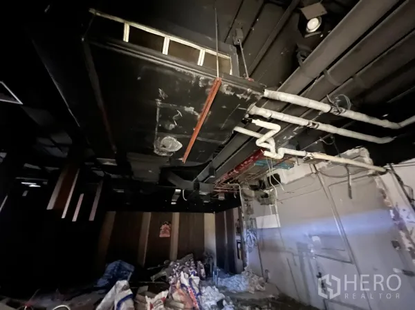 零售空间 出租 - 近距离展示裸顶中的机电管线与风管，地面有施工材料的毛坯零售空间。