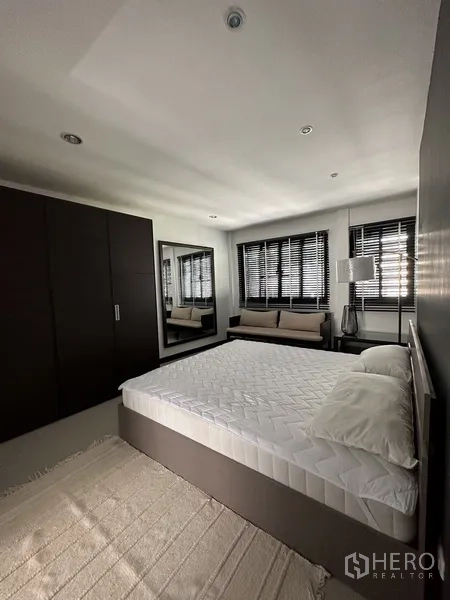 公寓 出租在Khlong Toei, Bangkok - 宽敞卧室，特大床、衣柜、窗边长凳与百叶窗。