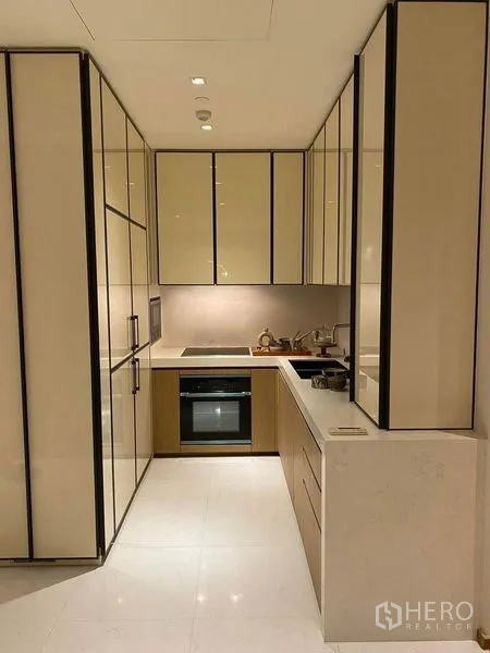 Condominium for rent or sale in Khlong Toei, Bangkok - Compact U-shaped kitchen with glossy cabinets, built-in oven and cooktop.