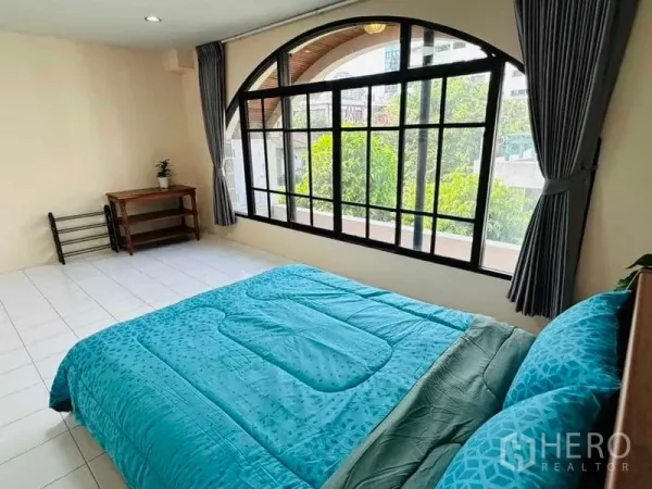 Home Office for rent - Bedroom with large arched window and garden view, dressed in teal bedding.