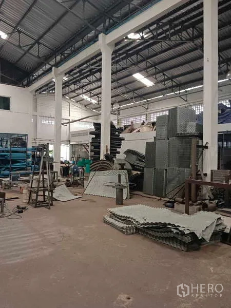 Warehouse for rent or sale in Nong Suea, Pathum Thani - High-clearance warehouse interior with columns and stacked materials.