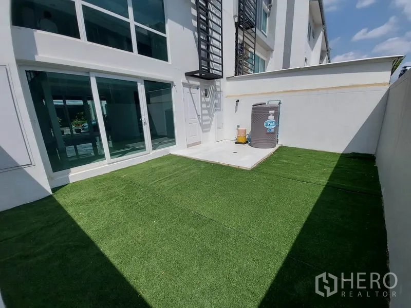ทาวน์เฮาส์ ขายในWang Thonglang, Bangkok - สวนส่วนตัวปูหญ้าเทียม ข้างตัวบ้านสีขาวพร้อมประตูกระจกบานเลื่อน