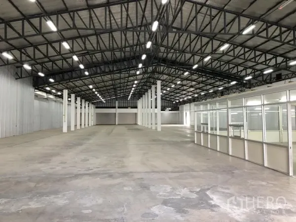 货栈 出租在Nonthaburi - 宽阔仓库地面，左侧金属包墙，右侧为办公室区块。