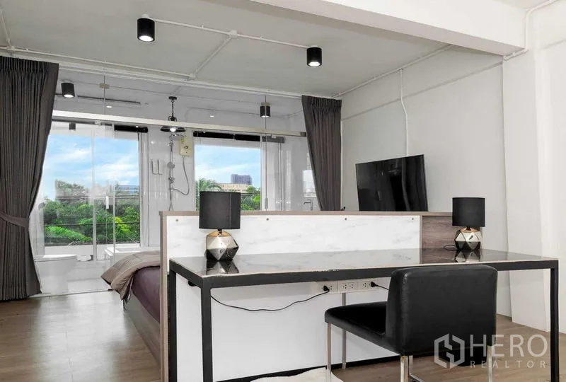 店屋 出售在Suan Luang, Bangkok - 明亮的工作室卧室，配书桌、电视与玻璃淋浴间，可见绿意景观。