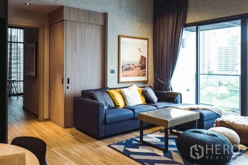 คอนโด ให้เช่าหรือขายในWatthana, Bangkok - ห้องนั่งเล่นสว่างด้วยพื้นไม้ โซฟาสีน้ำเงิน และระเบียงวิวเมือง