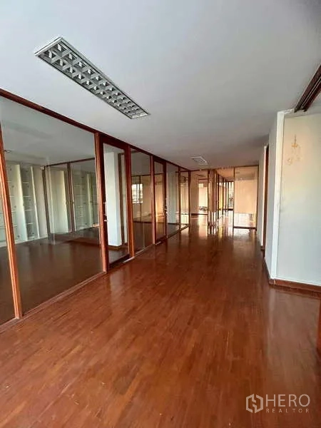 Home Office for rent or sale in Bang Phli, Samut Prakan - Extended hallway lined with multiple glass offices and wooden floors under fluorescent lighting.