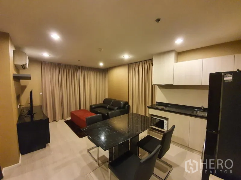 Condominium for rent in Sathon, Bangkok - Open-plan living, dining and kitchen at Rhythm Sathorn-Narathiwas with black dining table, beige curtains and modern cabinetry.