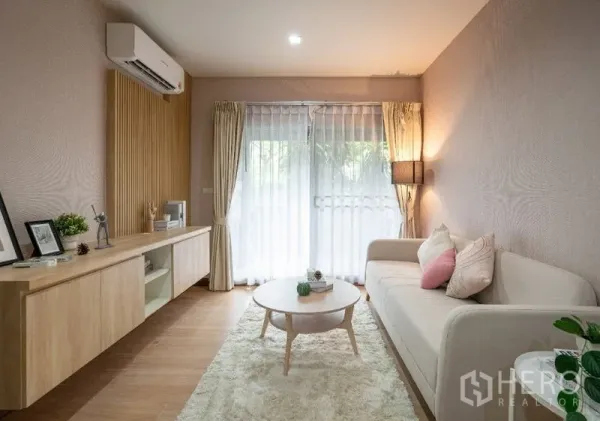 คอนโด ขาย - ห้องนั่งเล่นอบอุ่น พรมฟู โต๊ะกลางทรงกลม และแสงนุ่มจากม่านระเบียง