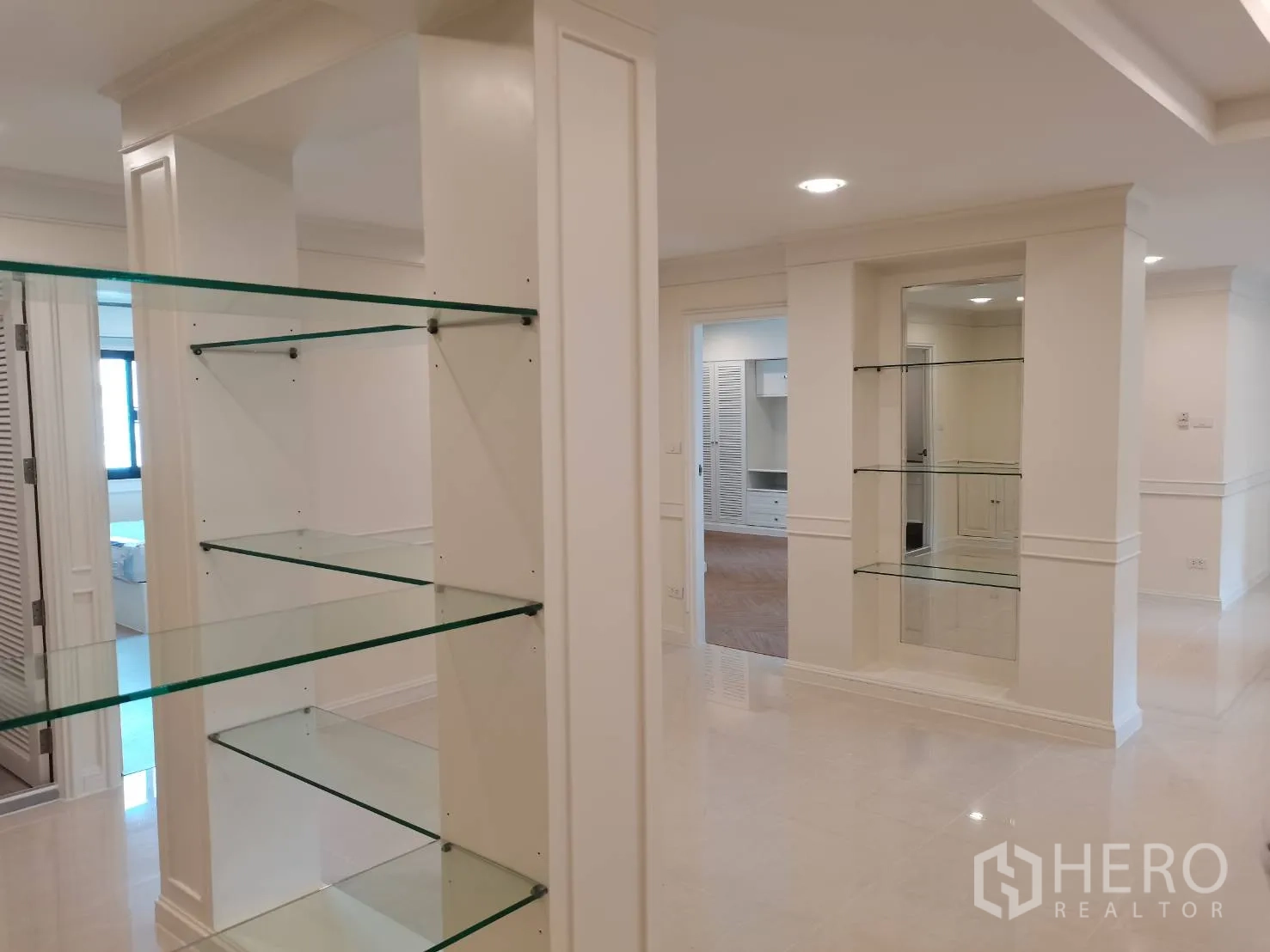 Condominium for rent in Watthana, Bangkok - Hallway with multiple glass shelving units leading to bedrooms.