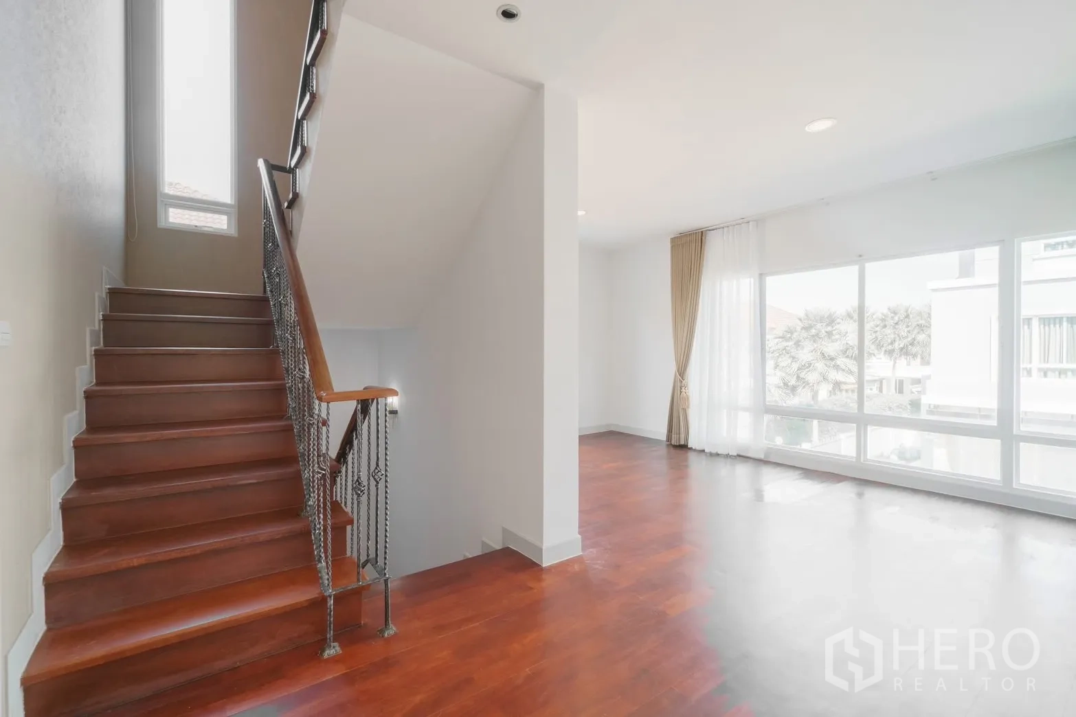 Detached House for rent or sale in Saphan Sung, Bangkok - Stairwell and family area with tall window and wood stairs.