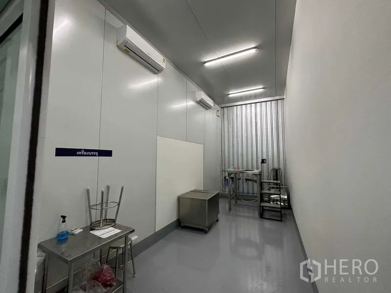 Factory for rent in Khlong Luang, Pathum Thani - Narrow packaging room with stainless benches, split AC units and easy-clean grey floor.