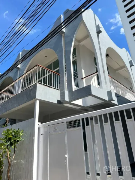 Home Office for rent in Watthana, Bangkok - Two-storey home office exterior with arched balconies and a gated entrance under a blue sky.