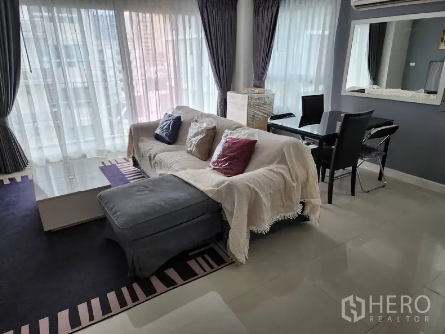 公寓 出租在Watthana, Bangkok - 采光充足的客餐厅，转角大窗，沙发与脚凳，玻璃餐桌。