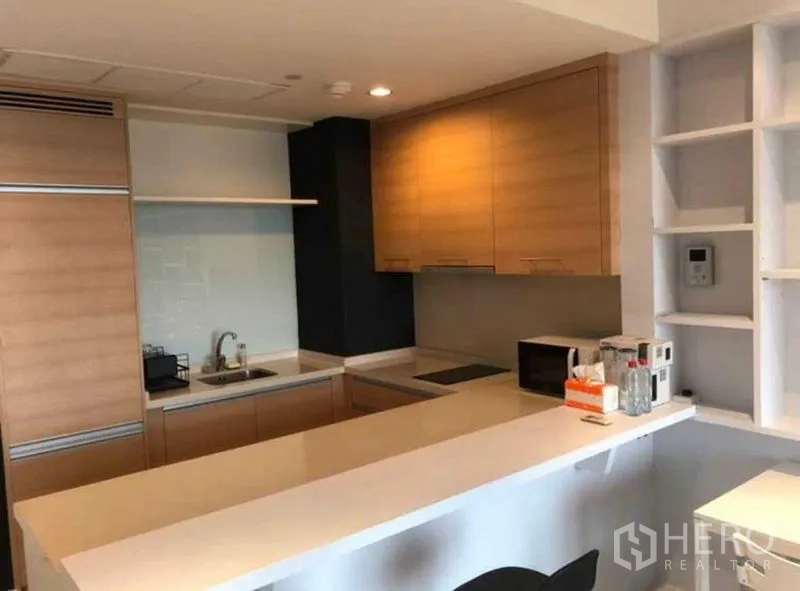 Condominium for sale in Khlong Toei, Bangkok - Compact kitchen featuring white countertop, cooktop, microwave and shelving.