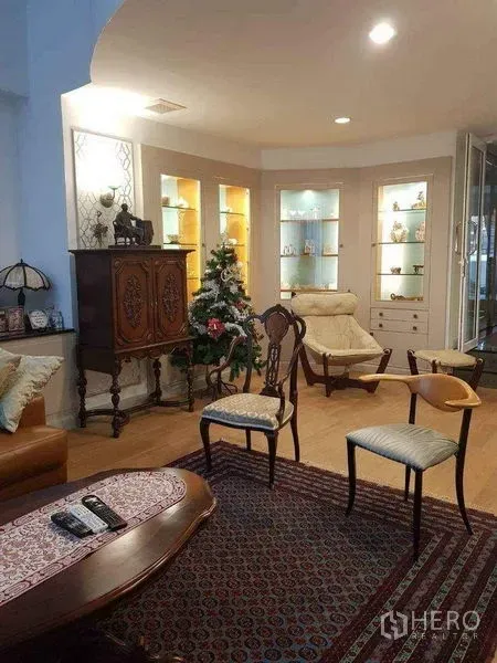 Townhouse for sale in Yan Nawa, Bangkok - Elegant living room with illuminated display shelves, antique cabinet, lounge chairs and rug.