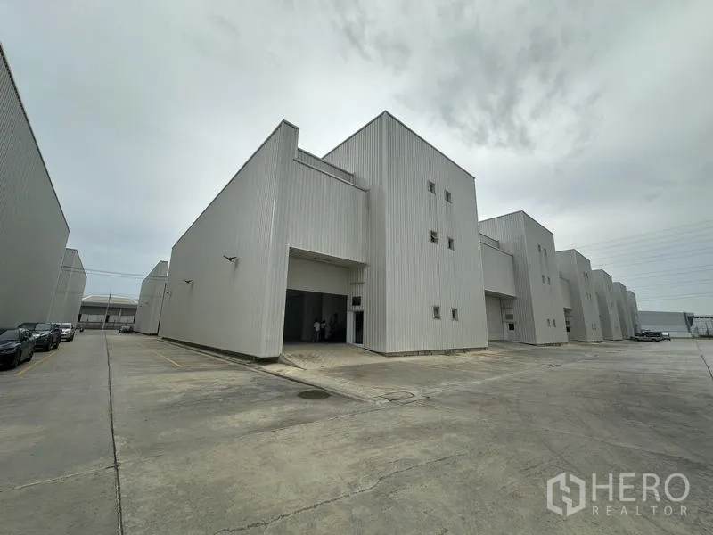 工厂 出租在Khlong Luang, Pathum Thani - 现代浅灰色厂房成排布局，宽阔混凝土车道便于卡车通行。