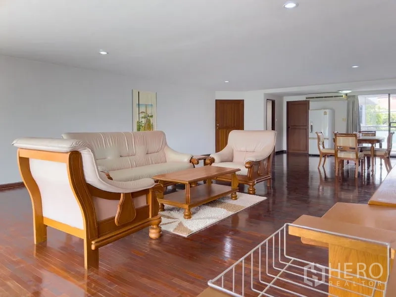 Condominium for sale in Samut Prakan - Open living room with sofa set and polished hardwood flooring next to dining area.