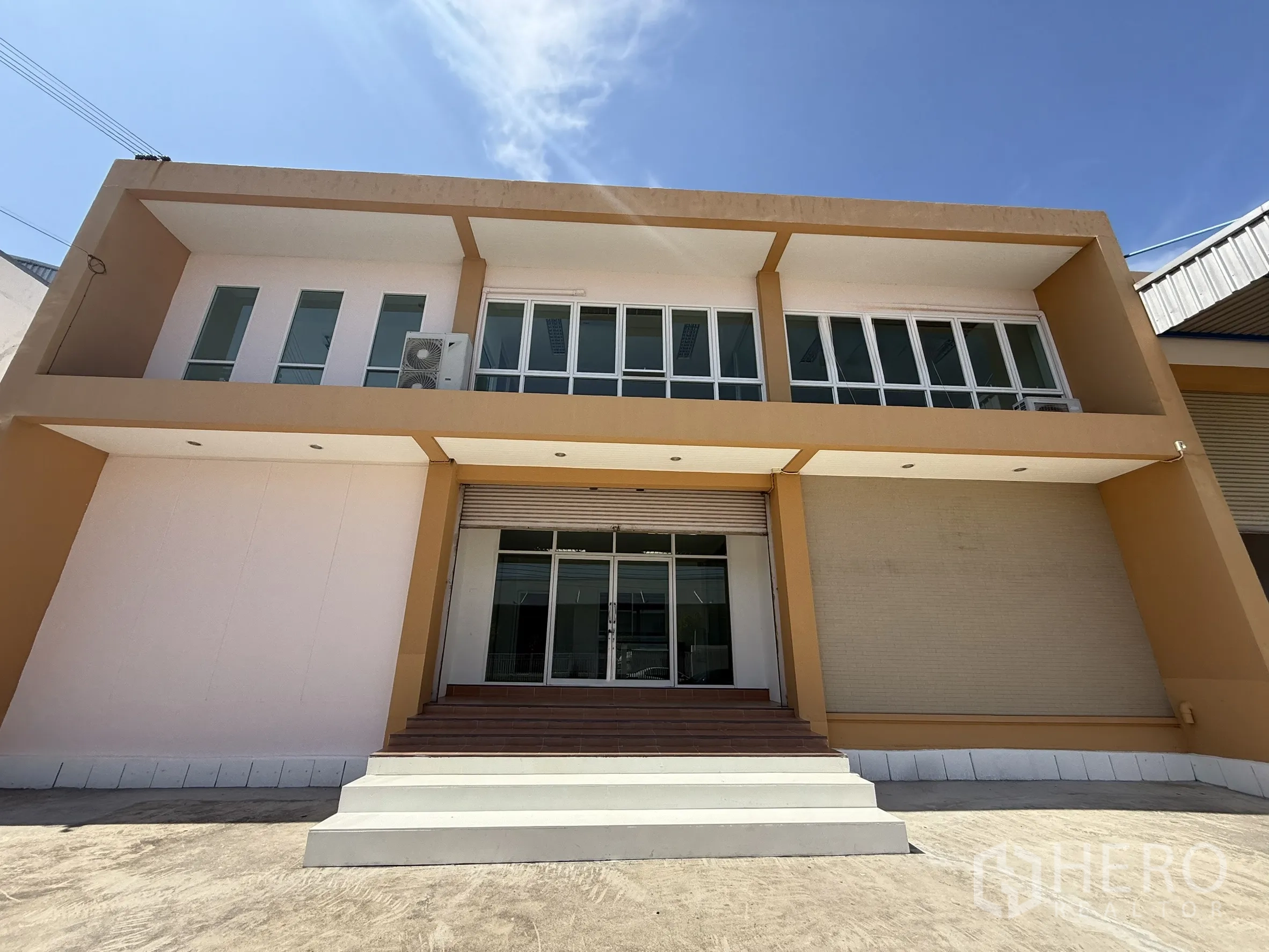 Warehouse for rent or sale in Bang Bo, Samut Prakan - Front facade of the office block with wide steps, glass entry and a roller shutter door.