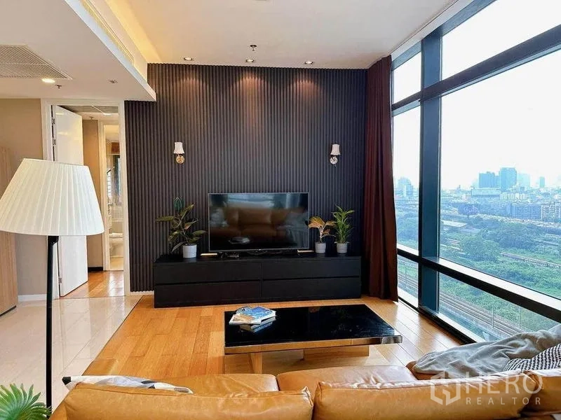 Condominium for rent in Ratchathewi, Bangkok - Modern living room with dark feature wall, TV console, wood floors, and floor-to-ceiling windows with panoramic Bangkok city views.