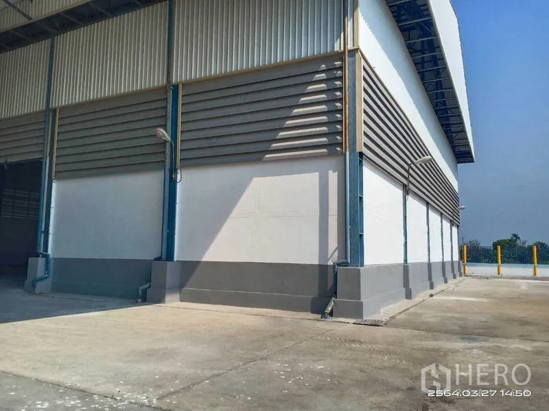 Warehouse for rent in Bang Bo, Samut Prakan - Exterior corner of the warehouse with a broad concrete yard and wall-mounted lighting.