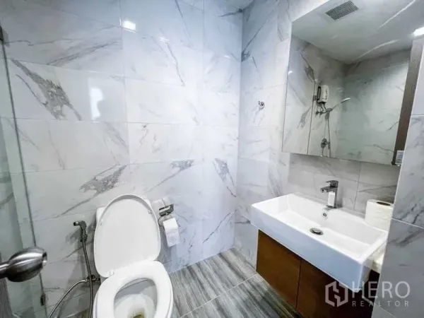 Condominium for sale in Huai Khwang, Bangkok - Modern bathroom featuring marble-look tiles, square basin with mirror cabinet and a toilet.