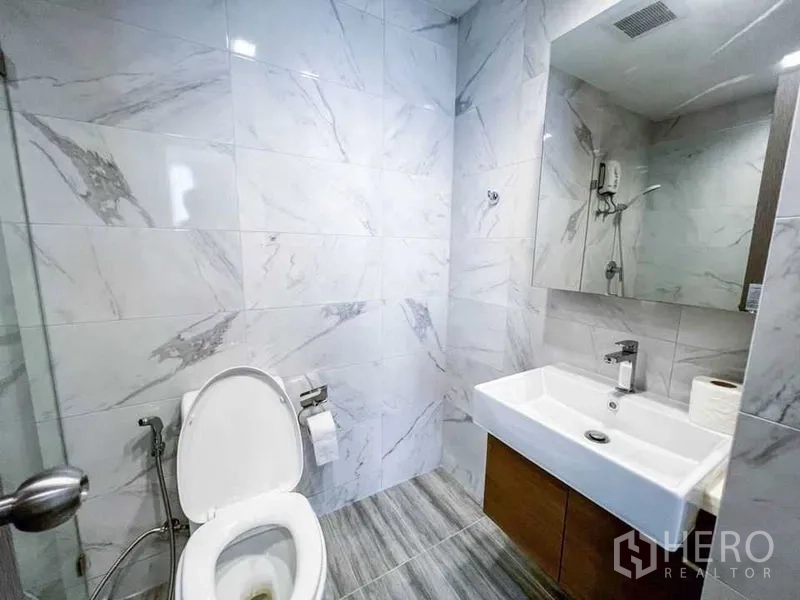 Condominium for sale in Huai Khwang, Bangkok - Modern bathroom featuring marble-look tiles, square basin with mirror cabinet and a toilet.