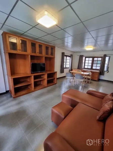 独立式住宅 出租在Nonthaburi - 客厅一角，转角沙发、电视柜与窗边餐桌。