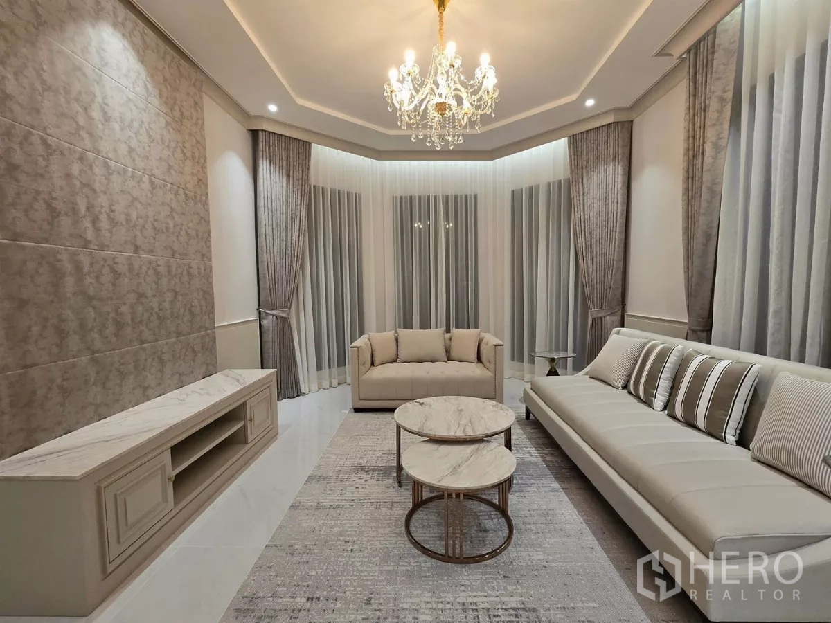 Detached House for rent or sale in Bang Kapi, Bangkok - Formal lounge with chandelier, large sofa set, built-in TV console and full-height curtains.