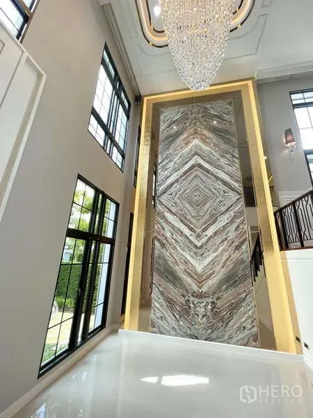 Detached House for sale in Thawi Watthana, Bangkok - Feature wall in the entrance hall clad in book-matched stone beneath a chandelier