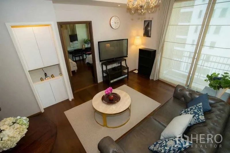 Condominium for rent in Watthana, Bangkok - Bright living room with chandelier, leather sofa, TV unit and floor-to-ceiling windows opening to a balcony.