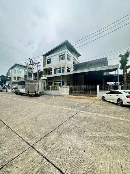 货栈 出租或出售在Lam Luk Ka, Pathum Thani - 更宽的街景视角，展示带围栏的仓库与邻近建筑。