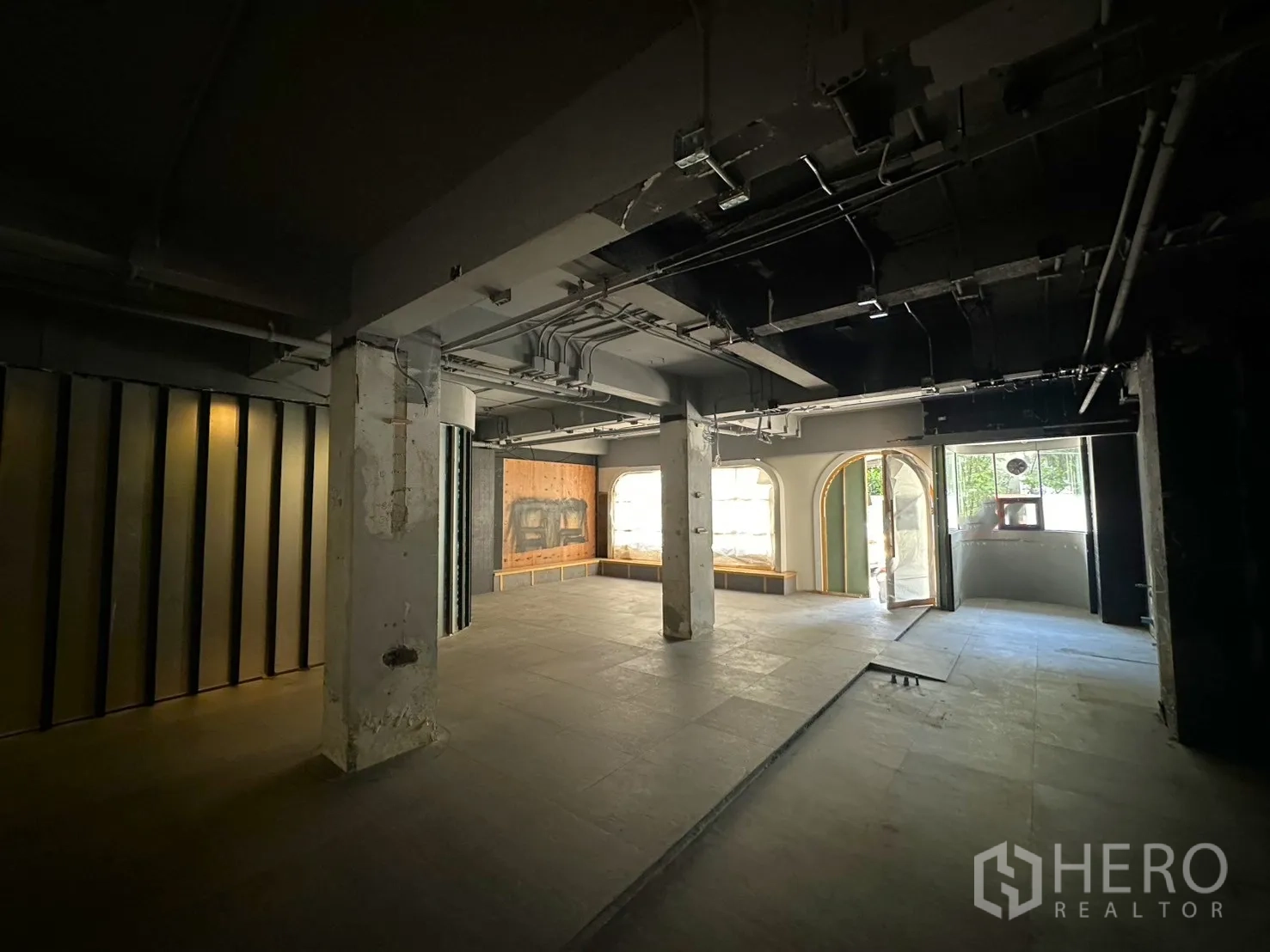 Retail Space for rent in Watthana, Bangkok - Interior looking to the storefront with an arched glass door, display windows, and unfinished floor.