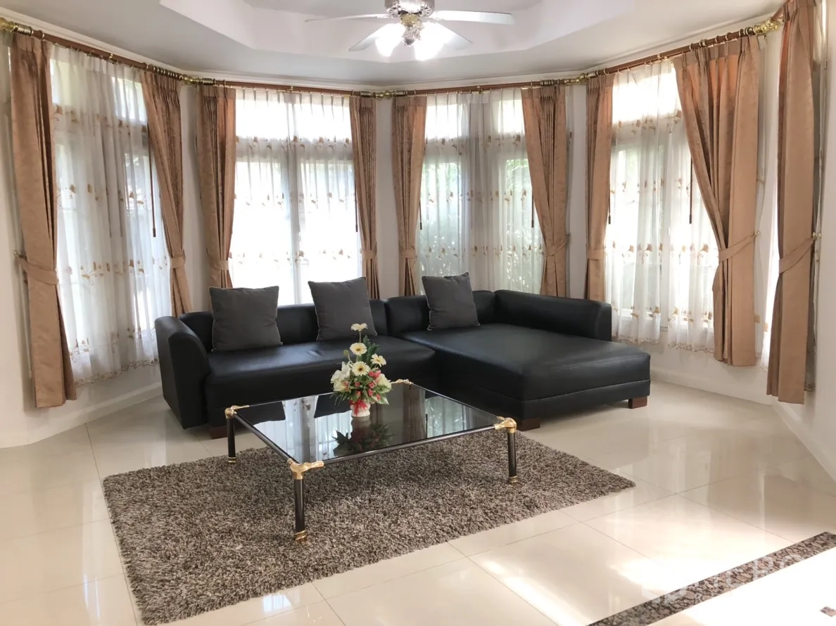 บ้าน ให้เช่าหรือขายในLat Phrao, Bangkok - ห้องนั่งเล่นสว่างไสว โซฟาเข้ามุมสีดำ โต๊ะกระจก หน้าต่างแบบเบย์และพัดลมเพดาน