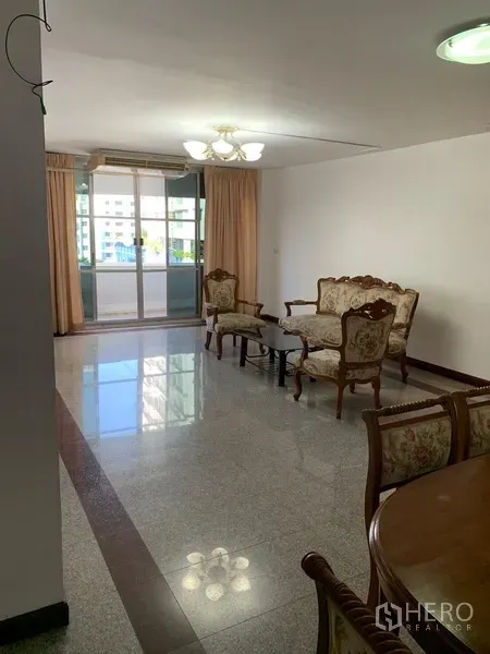 Condominium for rent in Sathon, Bangkok - Bright living room with large window, chandelier and classic sofa set opening to an enclosed balcony.