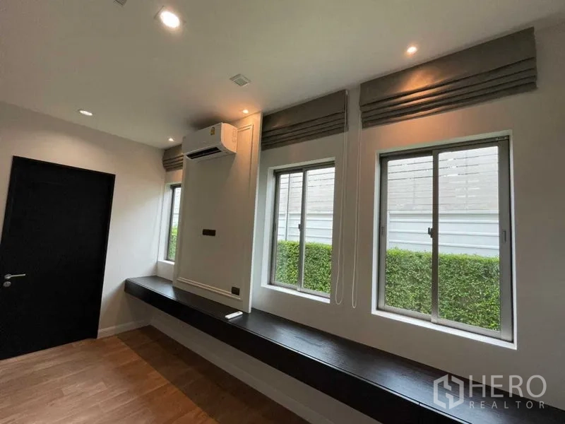 บ้าน ให้เช่าหรือขายในLat Krabang, Bangkok - ห้องนั่งเล่น/ทำงาน มีหน้าต่าง 3 บาน ม่านพับ แอร์ และม้านั่งบิลท์อิน มองเห็นแนวรั้วต้นไม้