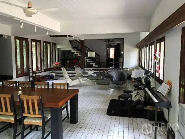 Detached House for rent in Khlong Toei, Bangkok - Spacious open-plan living area with many windows, tiled floor, and a statement staircase.
