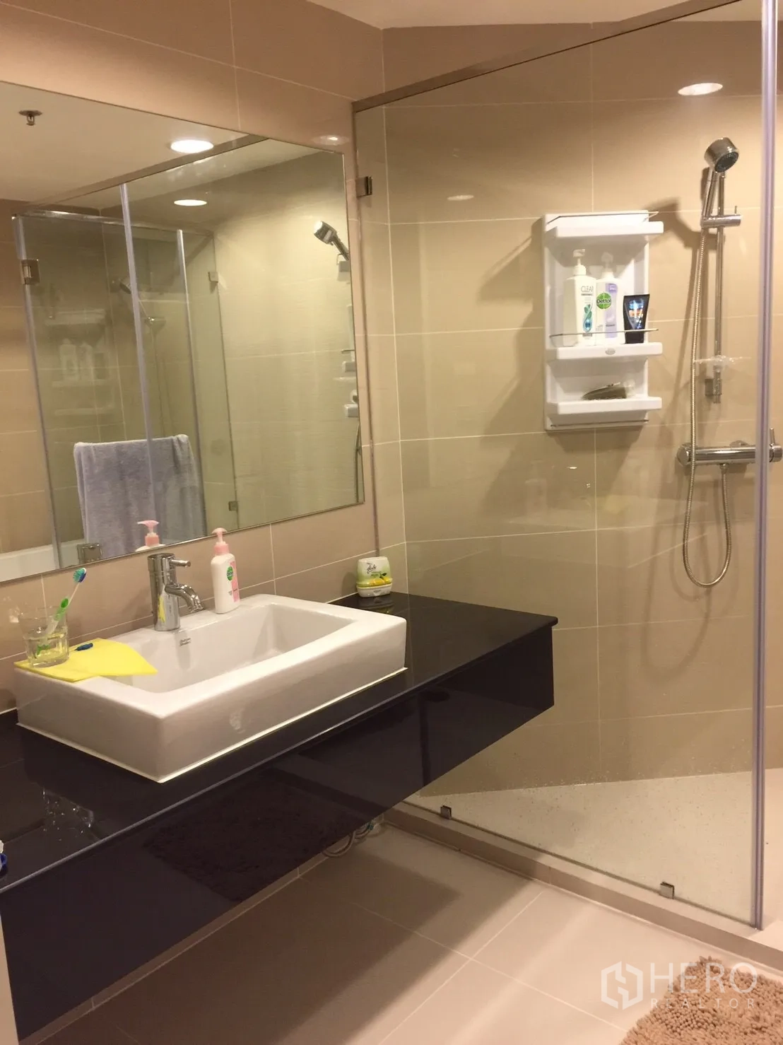 Condominium for rent in Huai Khwang, Bangkok - Bathroom with wide vanity, large mirror and glass-enclosed shower.