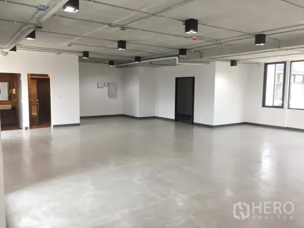 สำนักงาน ให้เช่าในKhlong Toei, Bangkok - พื้นที่สำนักงานกว้าง ผนังสีขาว ฝ้าเพดานเปลือยและโคมไฟ มีหน้าต่างหลายด้าน พร้อมประตูเข้าห้องน้ำ