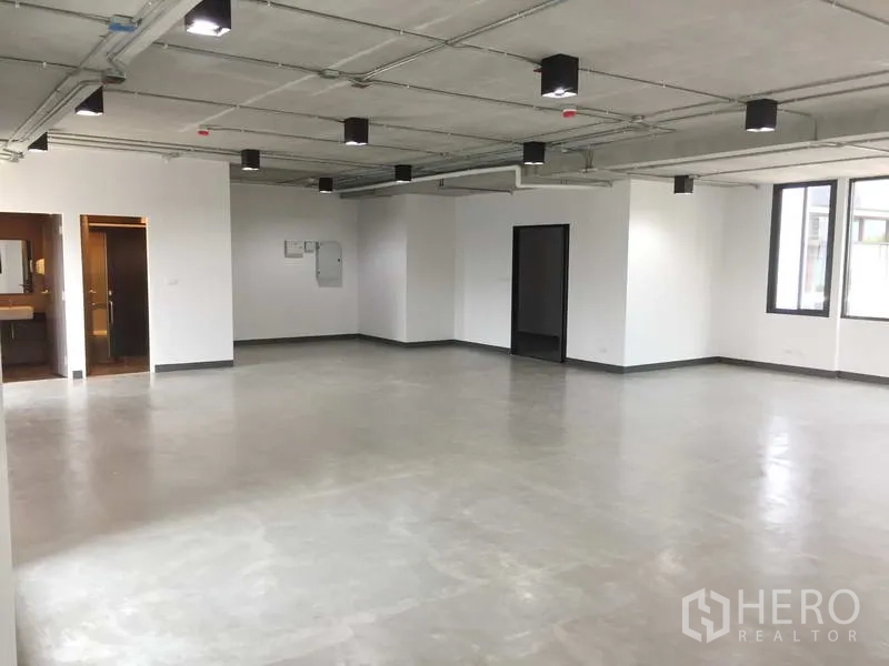 สำนักงาน ให้เช่าในKhlong Toei, Bangkok - พื้นที่สำนักงานกว้าง ผนังสีขาว ฝ้าเพดานเปลือยและโคมไฟ มีหน้าต่างหลายด้าน พร้อมประตูเข้าห้องน้ำ
