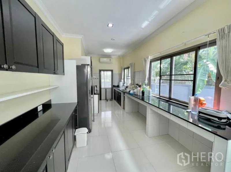 独立式住宅 出租在Prawet, Bangkok - 狭长型厨房，黑色石面台、大片窗户与后门。