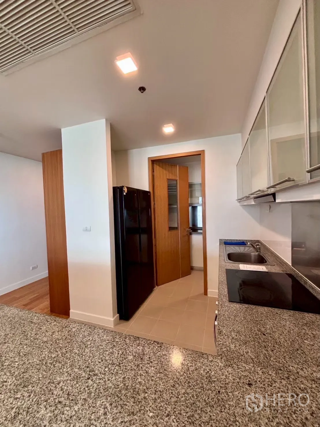 Condominium for rent in Khlong Toei, Bangkok - Kitchen view toward black refrigerator and granite counters
