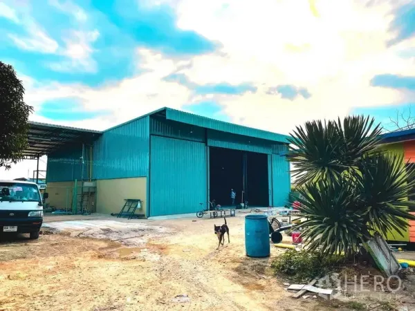 Warehouse for rent in Sai Mai, Bangkok - Street-side view of teal warehouse with wide driveway and perimeter wall.