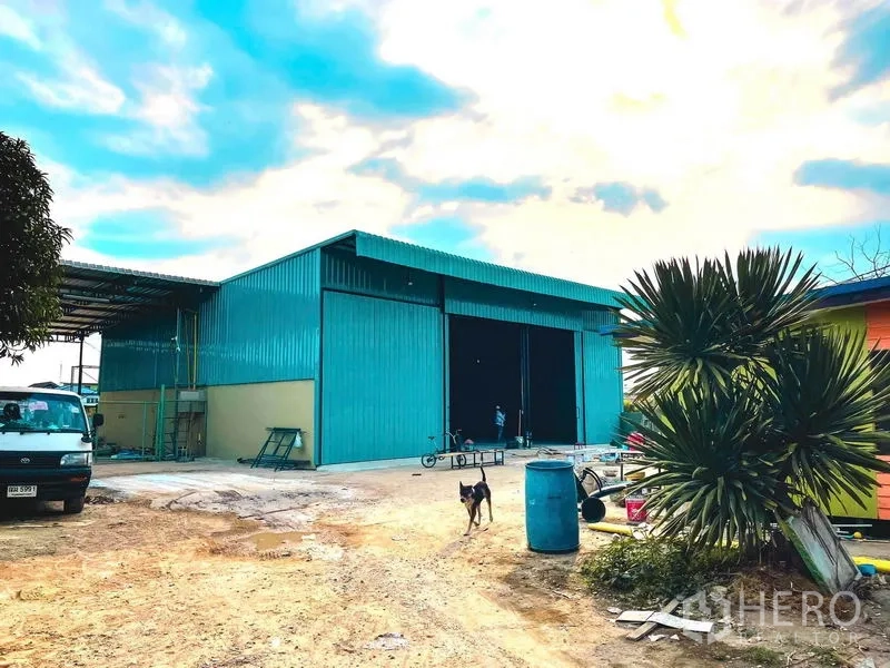 Warehouse for rent in Sai Mai, Bangkok - Street-side view of teal warehouse with wide driveway and perimeter wall.