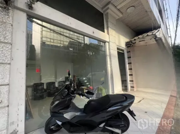 พื้นที่ขายปลีก ให้เช่า - มุมมองด้านข้างของทางเข้าหน้ากระจก พร้อมรถสกู๊ตเตอร์จอดริมทางเดินกระเบื้อง